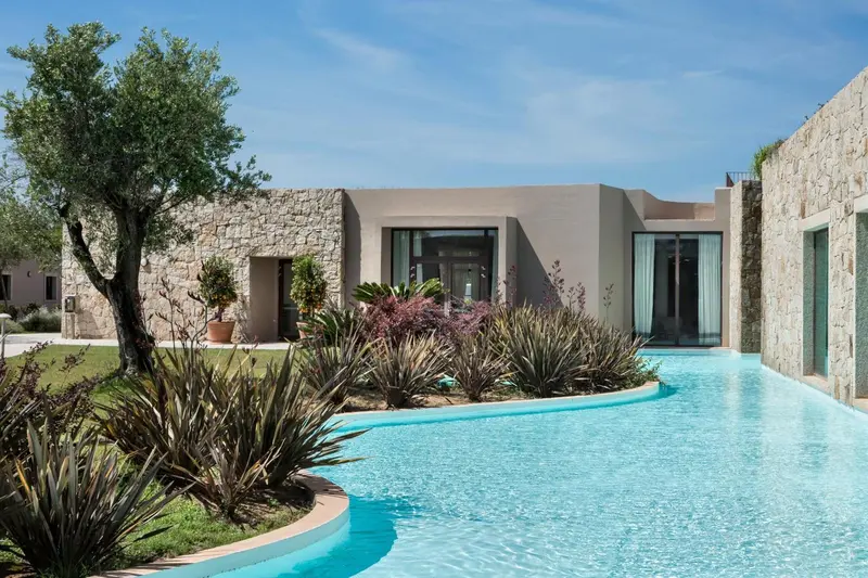 Une piscine sinueuse borde un bâtiment moderne aux murs clairs.