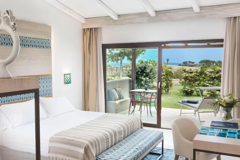 Une chambre lumineuse s'ouvre sur une terrasse avec vue sur la végétation et la mer.