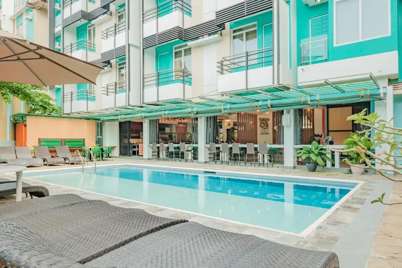 Une piscine turquoise bordée de chaises longues et d'une terrasse ombragée.