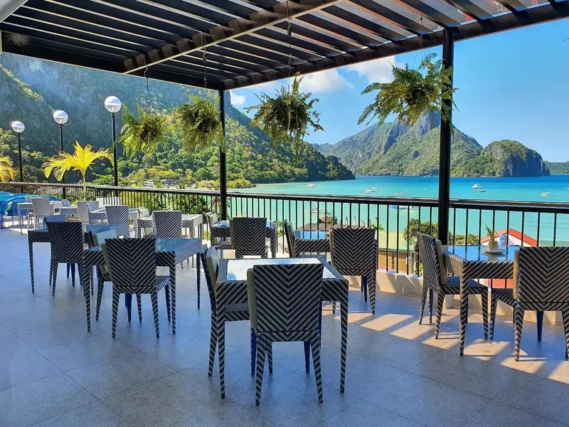 Terrasse ombragée avec tables et chaises donnant sur une vue marine.