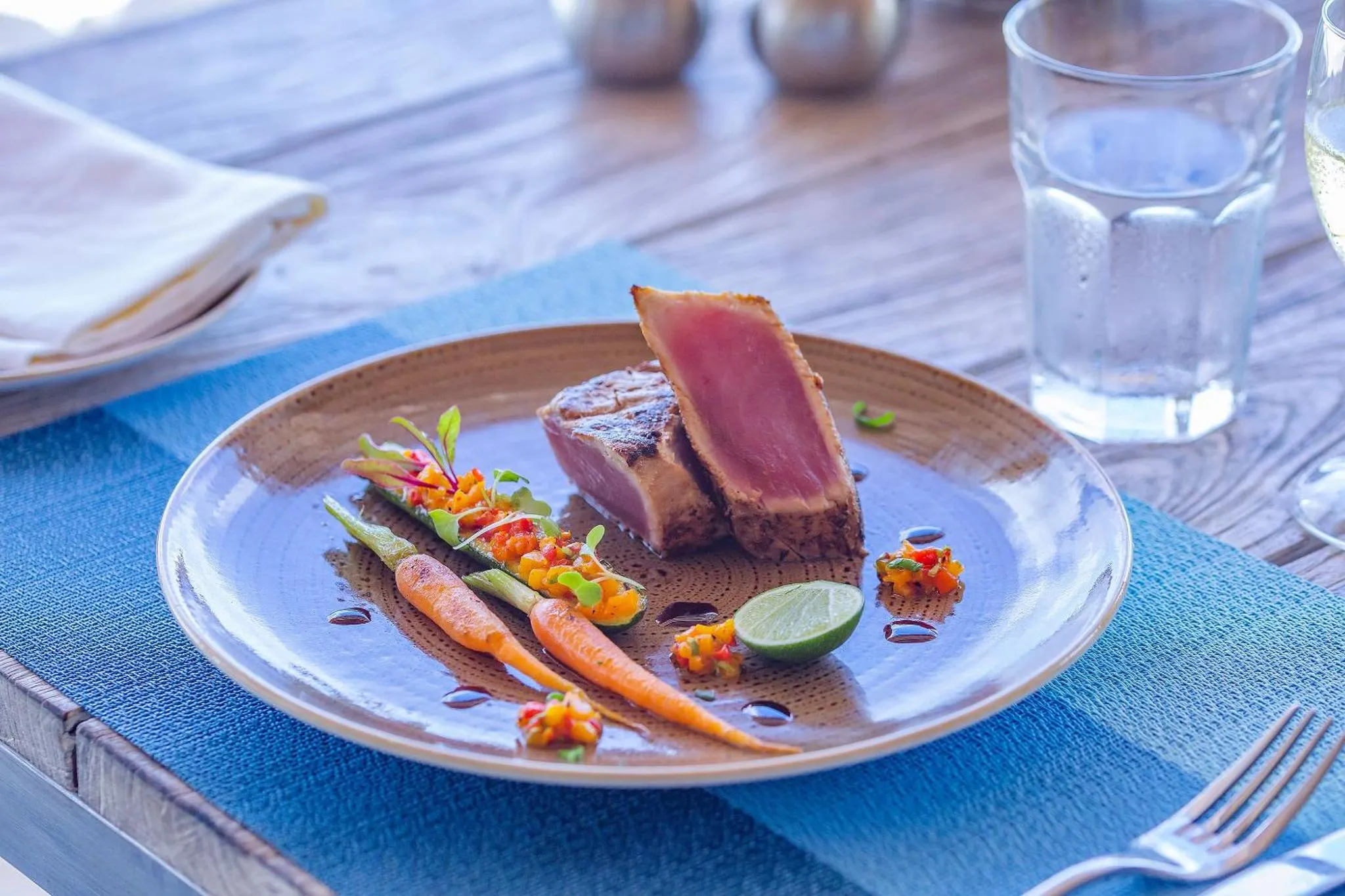 Assiette de poisson grillé décorée de légumes et d'herbes fraîches sur une table en bois.