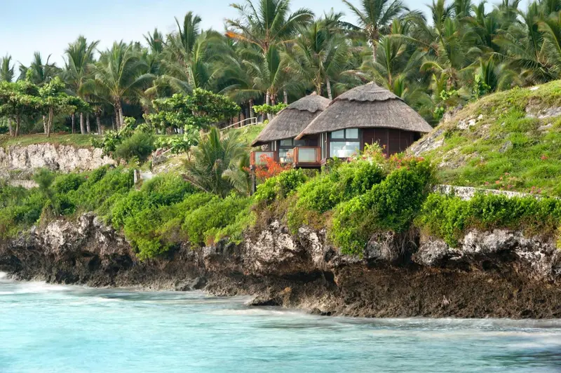 Des bungalows de chaume sont perchés sur une falaise surplombant une mer turquoise.
