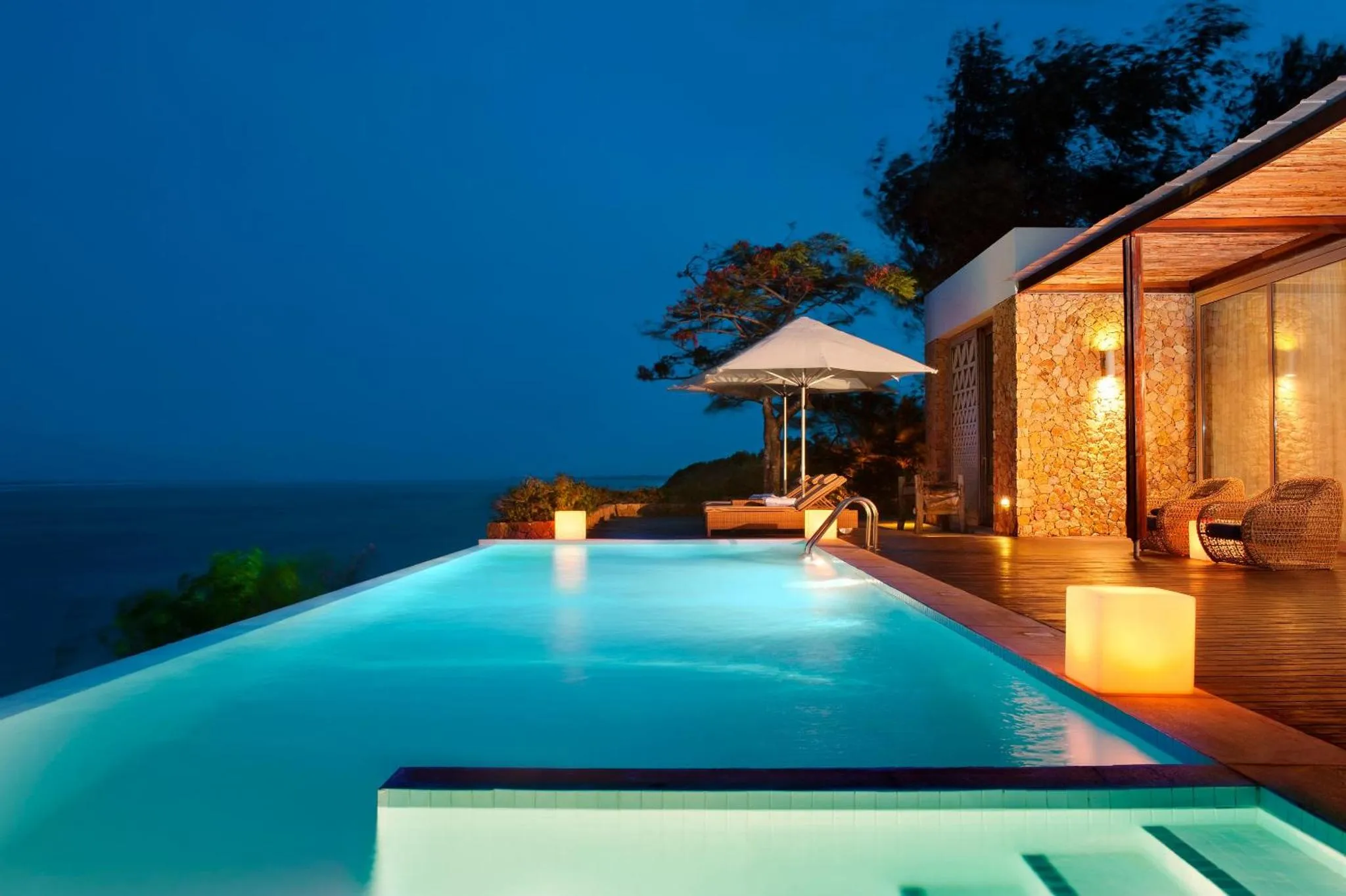 Piscine illuminée avec vue sur la mer au crépuscule.