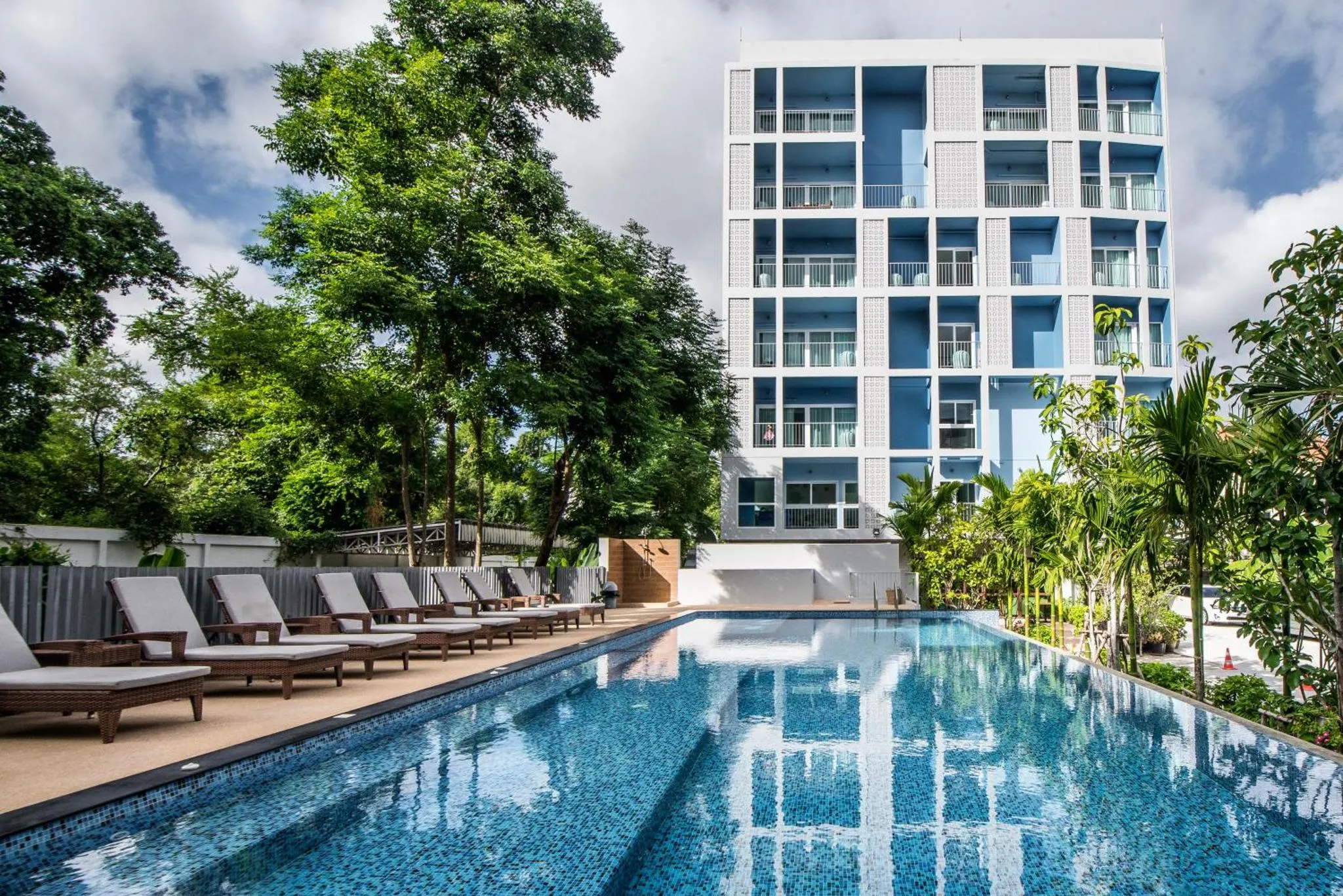 Bâtiment moderne blanc et bleu entouré de végétation, avec une piscine et des transats.