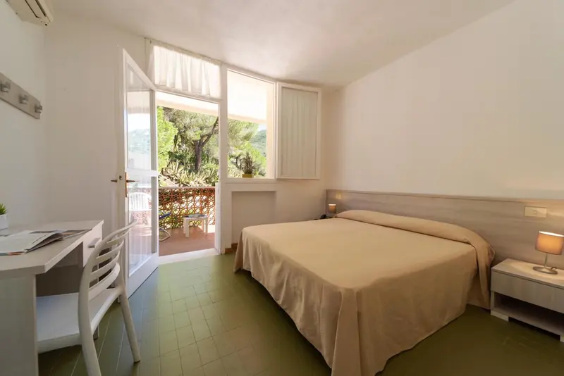 Une chambre lumineuse avec un lit et un bureau donnant sur une terrasse.