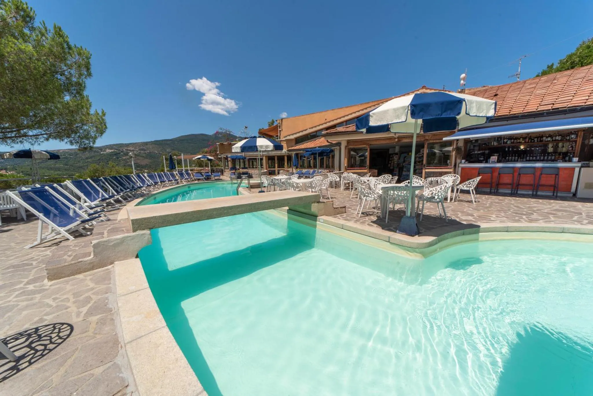 Piscine avec transats et bar en terrasse sous des parasols.