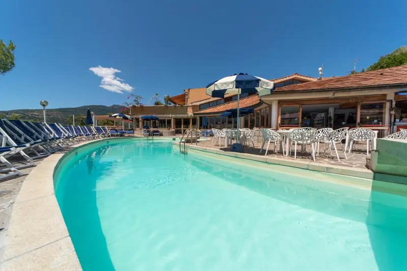 Une piscine turquoise bordée de transats sous des parasols colorés, avec un bâtiment en arrière-plan.