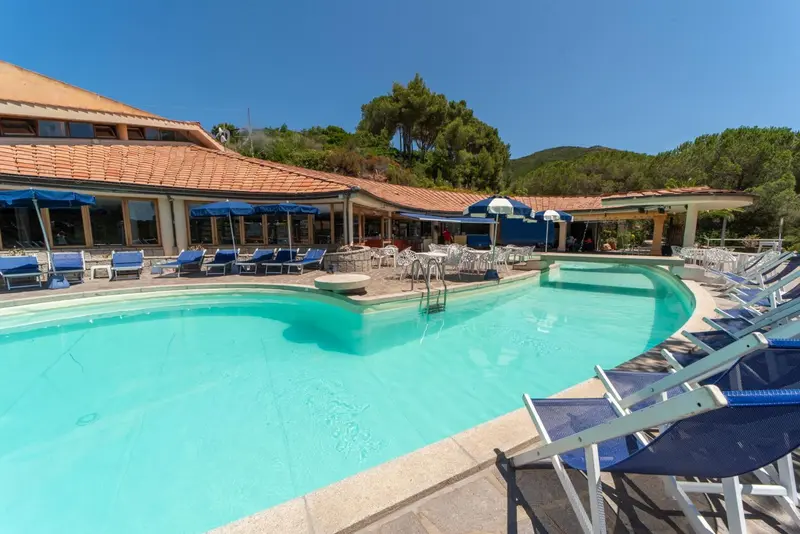 Une piscine rectangulaire avec des transats bleus et un bâtiment en arrière-plan.