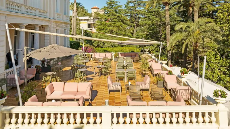 Terrasse ombragée avec tables et canapés roses.