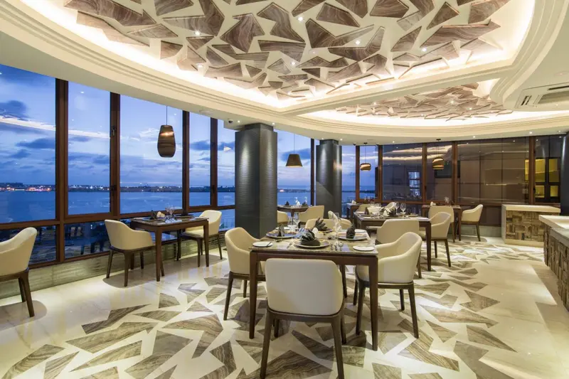 Une salle de restaurant lumineuse avec de grandes baies vitrées donnant sur une vue nocturne.