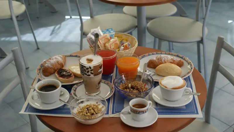 Une table ronde présente un petit-déjeuner avec des viennoiseries, des boissons et des céréales.