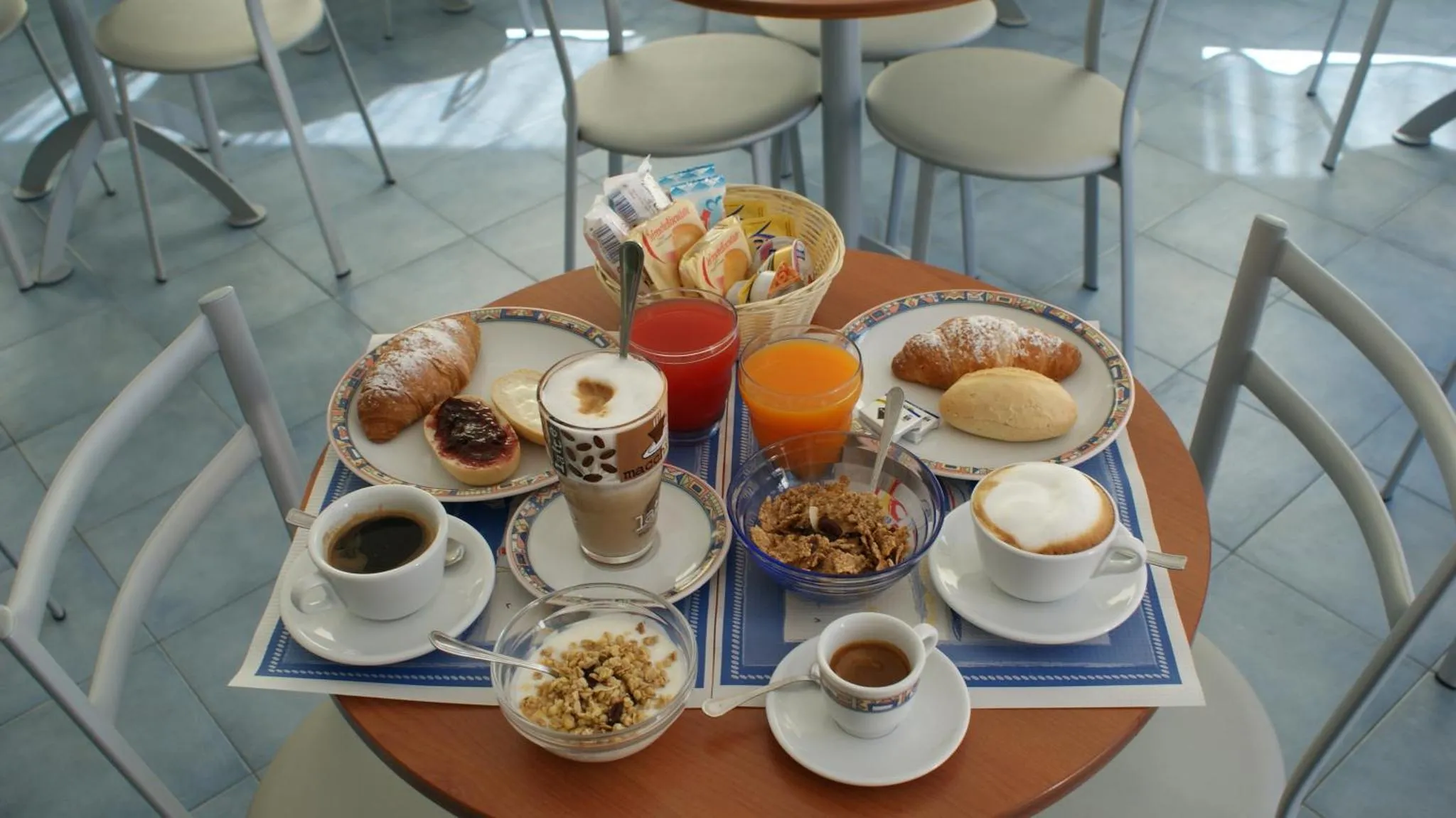 Une table ronde est dressée pour le petit-déjeuner avec des viennoiseries, des boissons et des céréales.