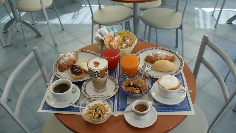 Une table ronde est dressée pour le petit-déjeuner avec des viennoiseries, des boissons et des céréales.