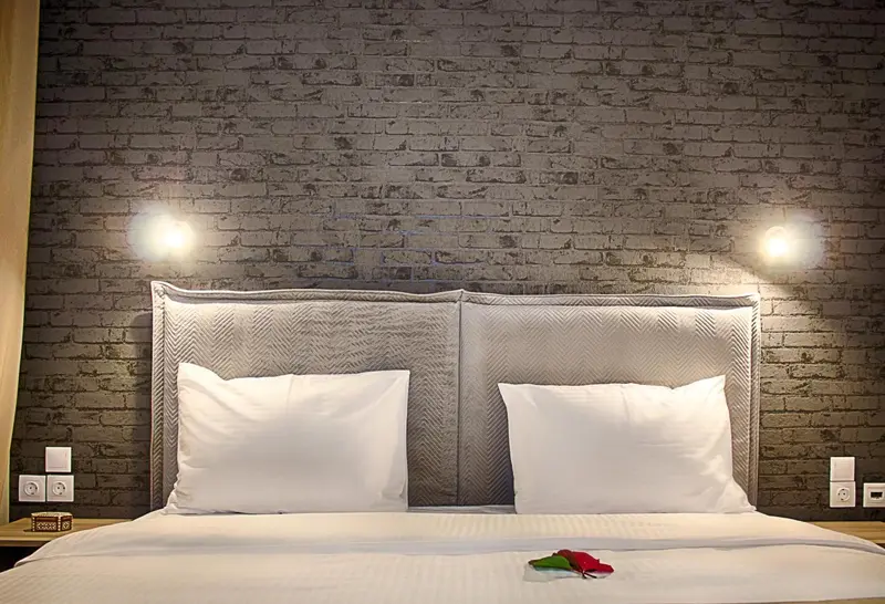 Un lit double avec des oreillers blancs se trouve devant un mur en imitation brique.