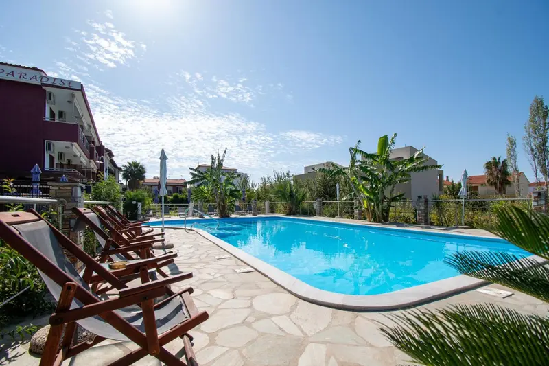 Transats alignés au bord d'une piscine turquoise dans un jardin soigné.