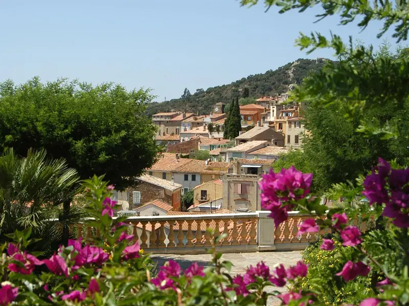 Vue d'un village sur une colline, encadrée par une végétation fleurie et une balustrade.