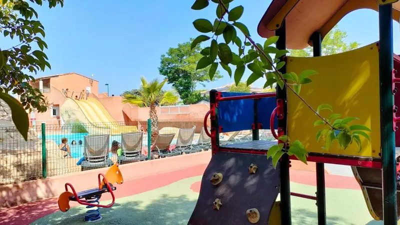 Aire de jeux colorée avec toboggan et structures d'escalade près d'une piscine.