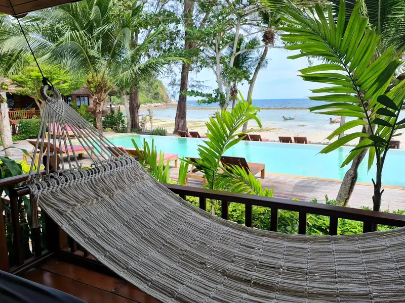 Un hamac est suspendu sur une terrasse en bois donnant sur une piscine et la mer.