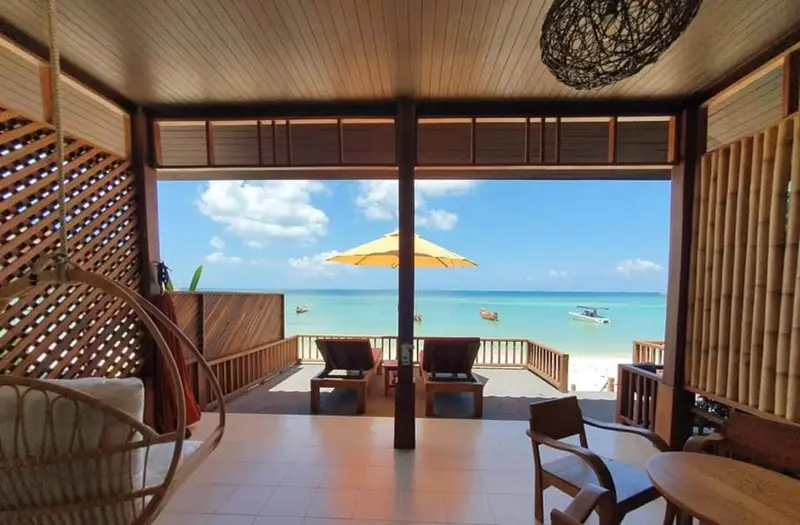 Terrasse en bois donnant sur une plage de sable blanc et une mer turquoise.
