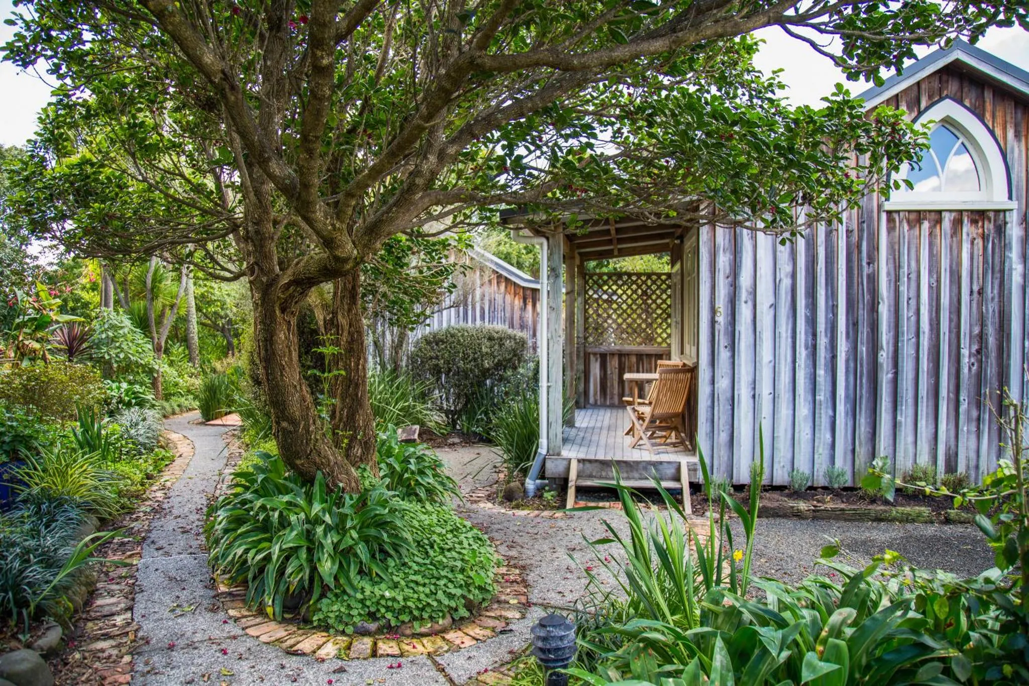 Un chemin mène à une petite maison en bois avec une terrasse ombragée.
