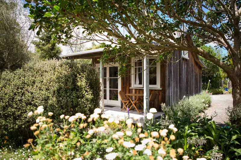 Petite maison en bois avec une terrasse fleurie et un jardin soigné.