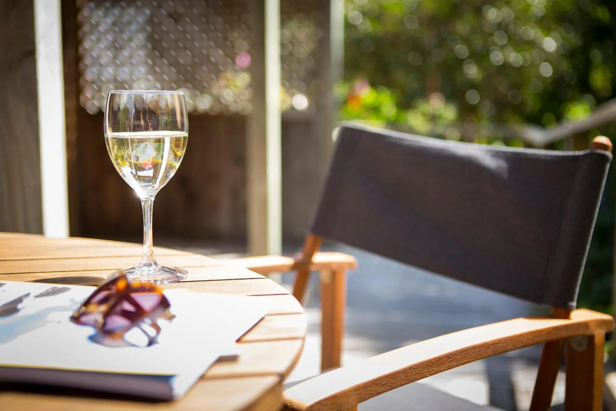 Un verre de vin et des lunettes de soleil reposent sur une table en bois près d'une chaise.