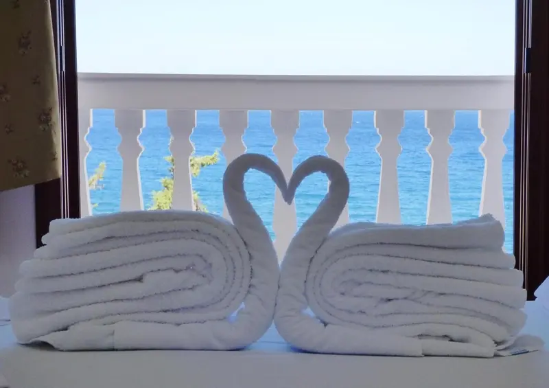 Serviettes pliées en forme de cygnes sur un lit avec vue sur la mer.
