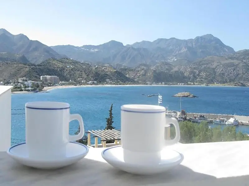Deux tasses de café sur une terrasse ensoleillée avec vue sur la mer et les montagnes.