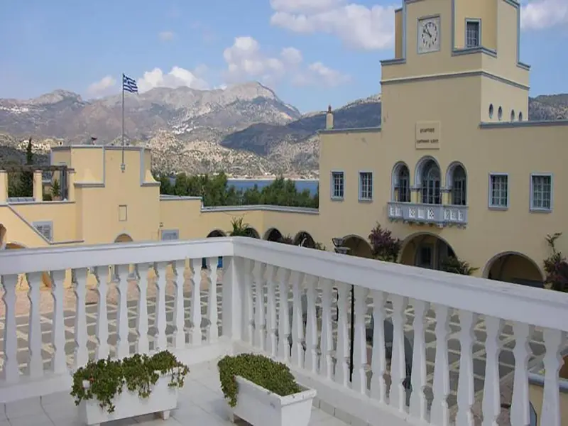 Balcon fleuri donnant sur un bâtiment jaune et des montagnes.