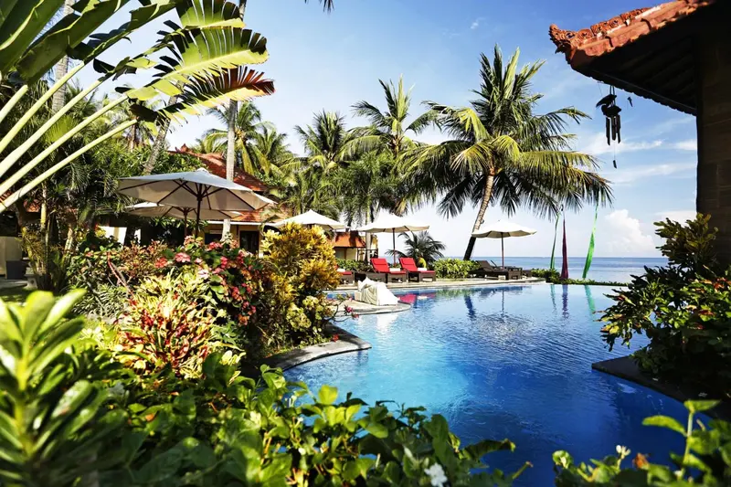Une piscine bleue bordée de végétation luxuriante et de chaises longues.