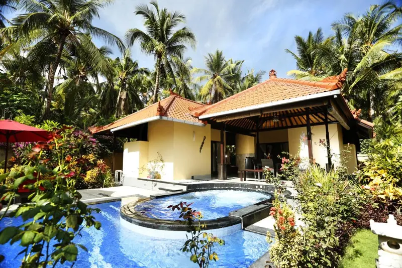 Petite piscine devant un bâtiment aux toits rouges et aux murs jaunes, entouré de végétation tropicale.