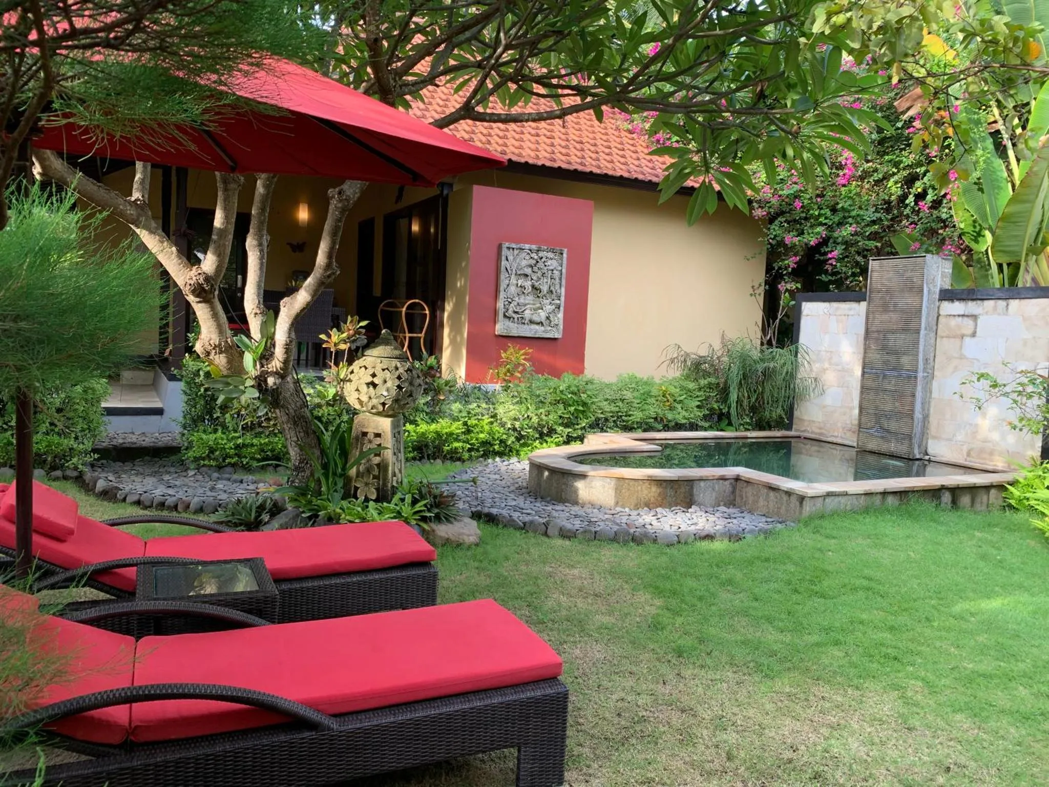Transats rouges disposés devant un jardin tropical et une petite piscine.