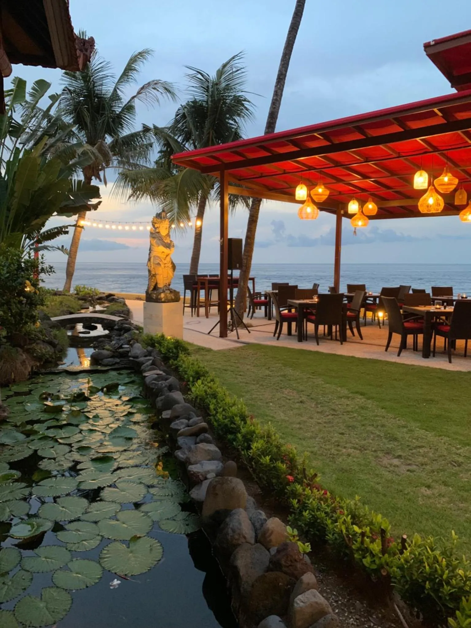 Terrasse ombragée avec tables et chaises face à la mer.