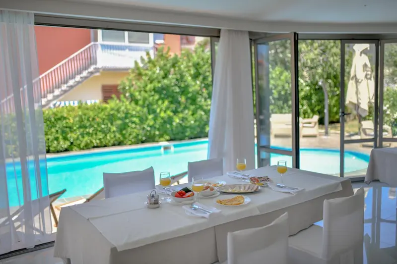 Une table est dressée pour le petit-déjeuner devant de grandes baies vitrées donnant sur une piscine.
