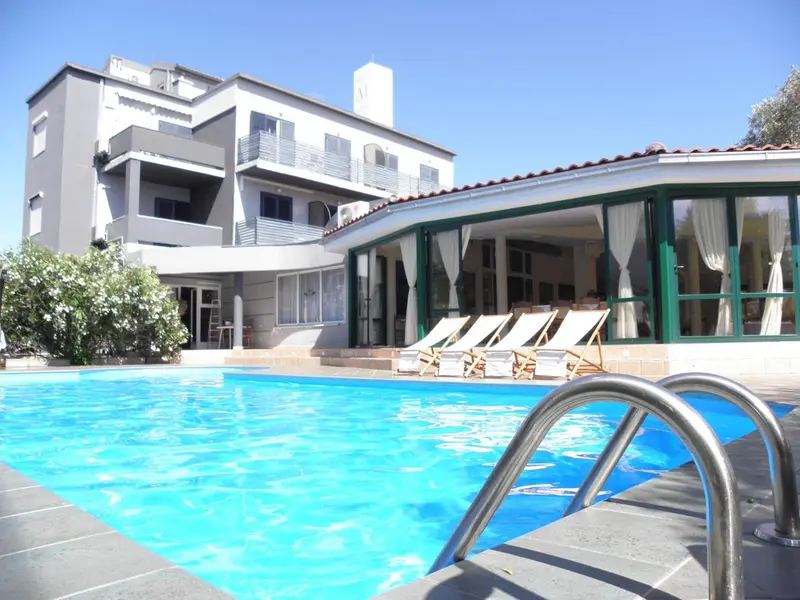 Une piscine turquoise au premier plan, avec des transats et un bâtiment blanc à l'arrière-plan.
