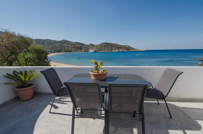 Une table et des chaises en métal sur une terrasse ensoleillée avec vue sur la mer.