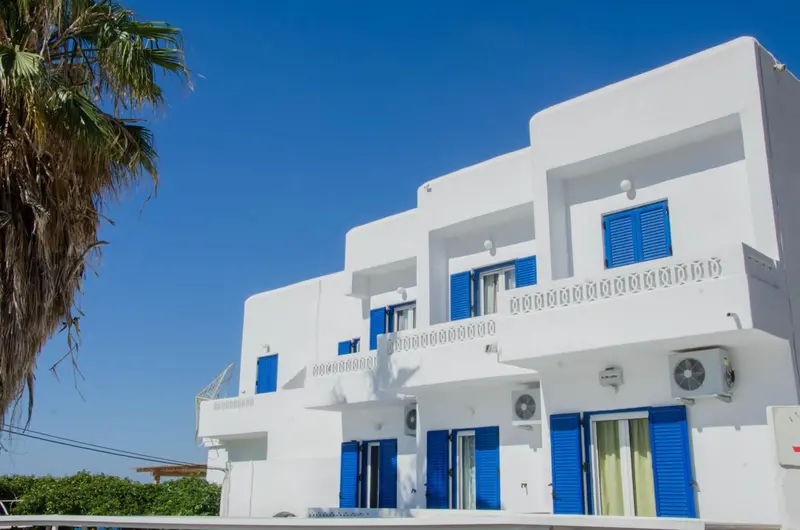 Bâtiment blanc aux fenêtres et balcons bleus sous un ciel clair.