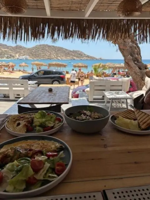 Une table en bois présente des assiettes garnies en terrasse avec vue sur la mer.