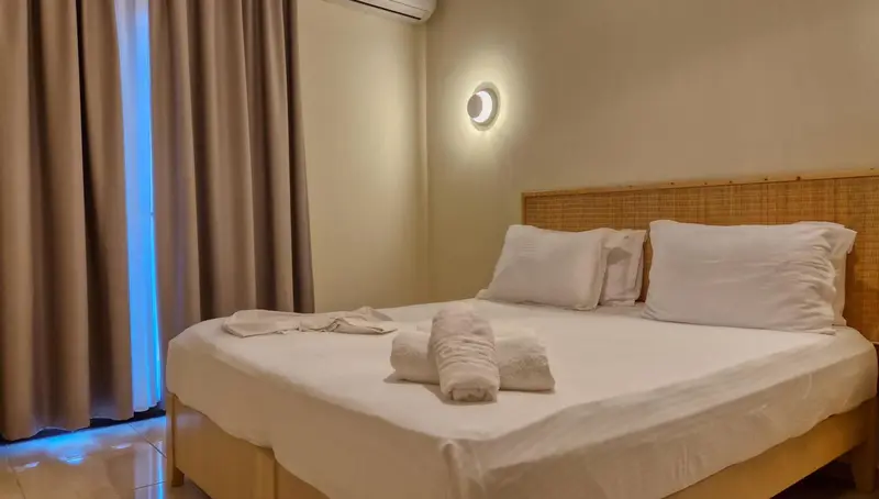 Une chambre lumineuse avec un grand lit recouvert de draps blancs et des rideaux beiges.
