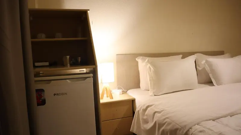 Une chambre lumineuse avec un lit fait et un petit réfrigérateur.