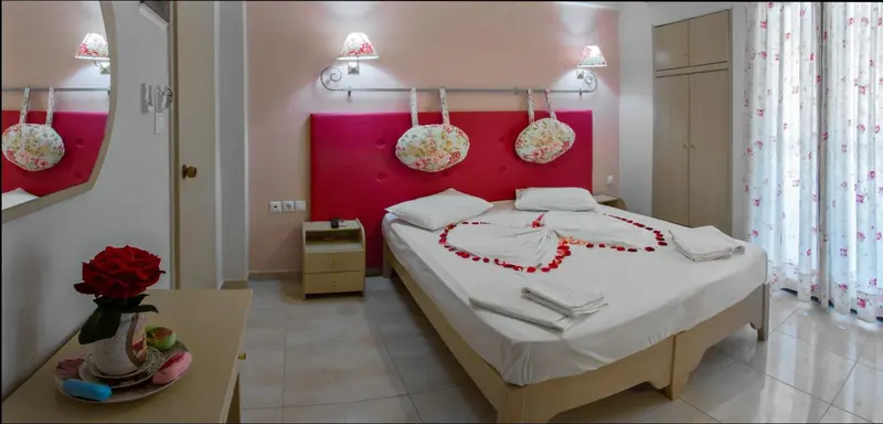 Une chambre d'hotel avec un lit decoré de pétales de roses et de serviettes en forme de cœur.