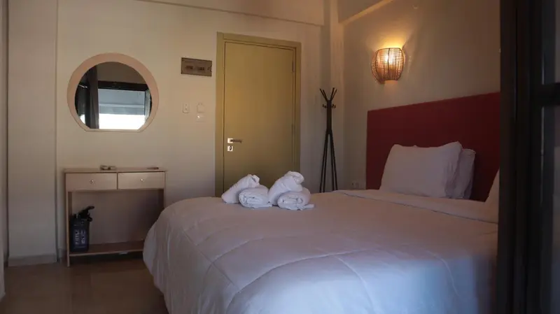 Une chambre lumineuse avec un lit recouvert d'une couette blanche et un miroir rond au mur.