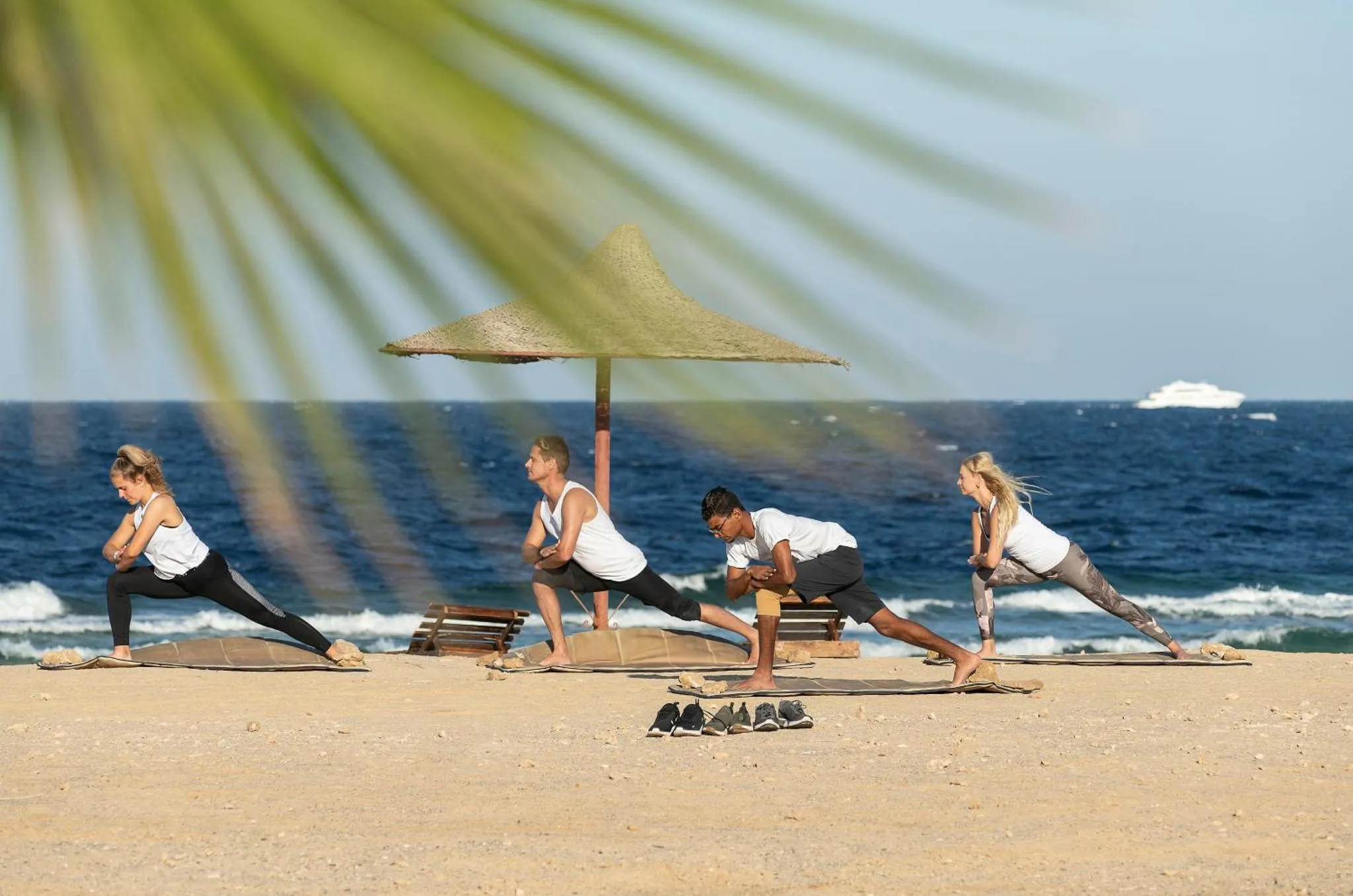 Personnes pratiquant le yoga sur une plage de sable fin face à la mer.