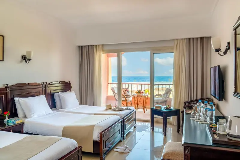 Une chambre lumineuse avec deux lits et une vue sur la mer par de grandes baies vitrées.