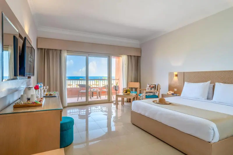Chambre lumineuse avec un lit double et une vue sur la mer depuis un balcon.