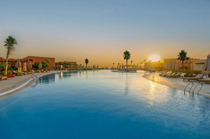 Une grande piscine turquoise reflète le ciel orangé du coucher de soleil.