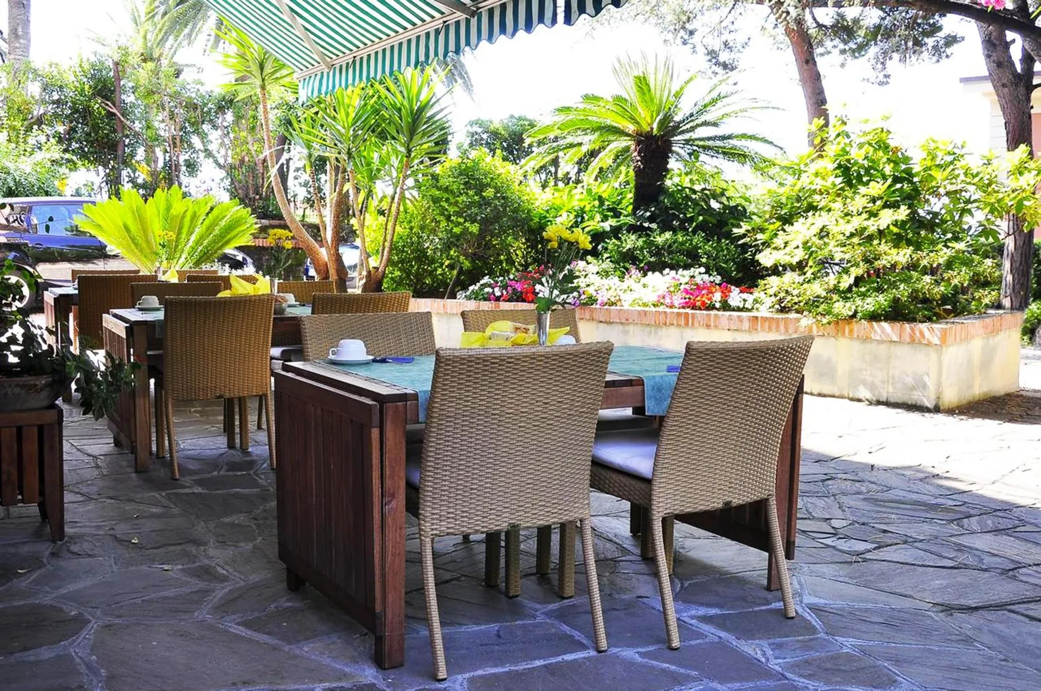 Tables et chaises en osier disposées sur une terrasse pavée ombragée par une marquise.