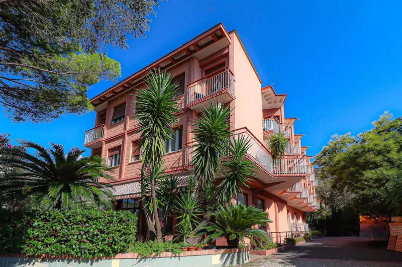 Façade d'un bâtiment rose à plusieurs étages avec des balcons et de la végétation.