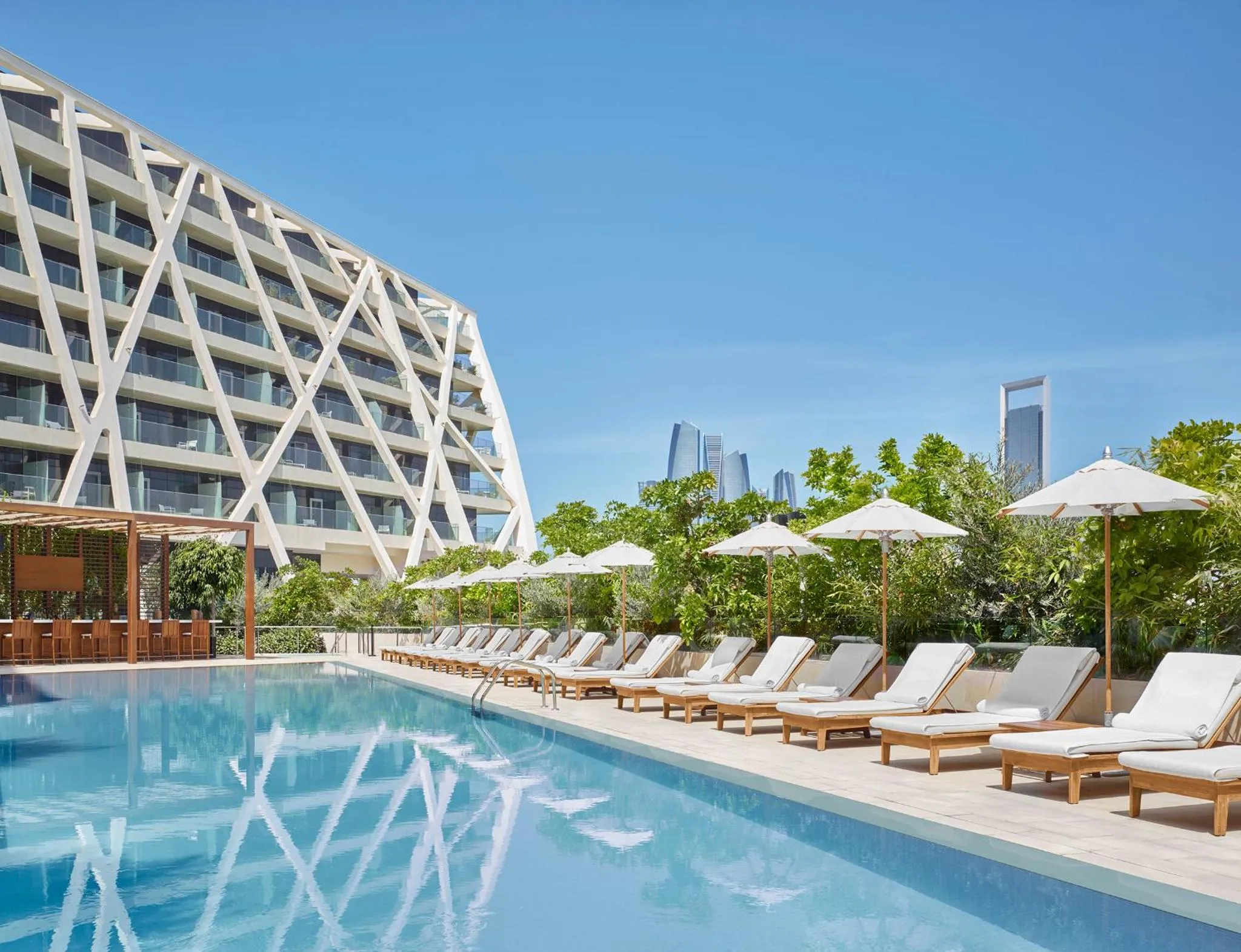 Une piscine rectangulaire bordée de transats blancs sous des parasols.