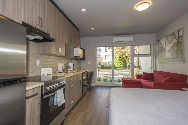Une kitchenette moderne s'ouvre sur un espace de vie avec un canapé rouge et une fenêtre.